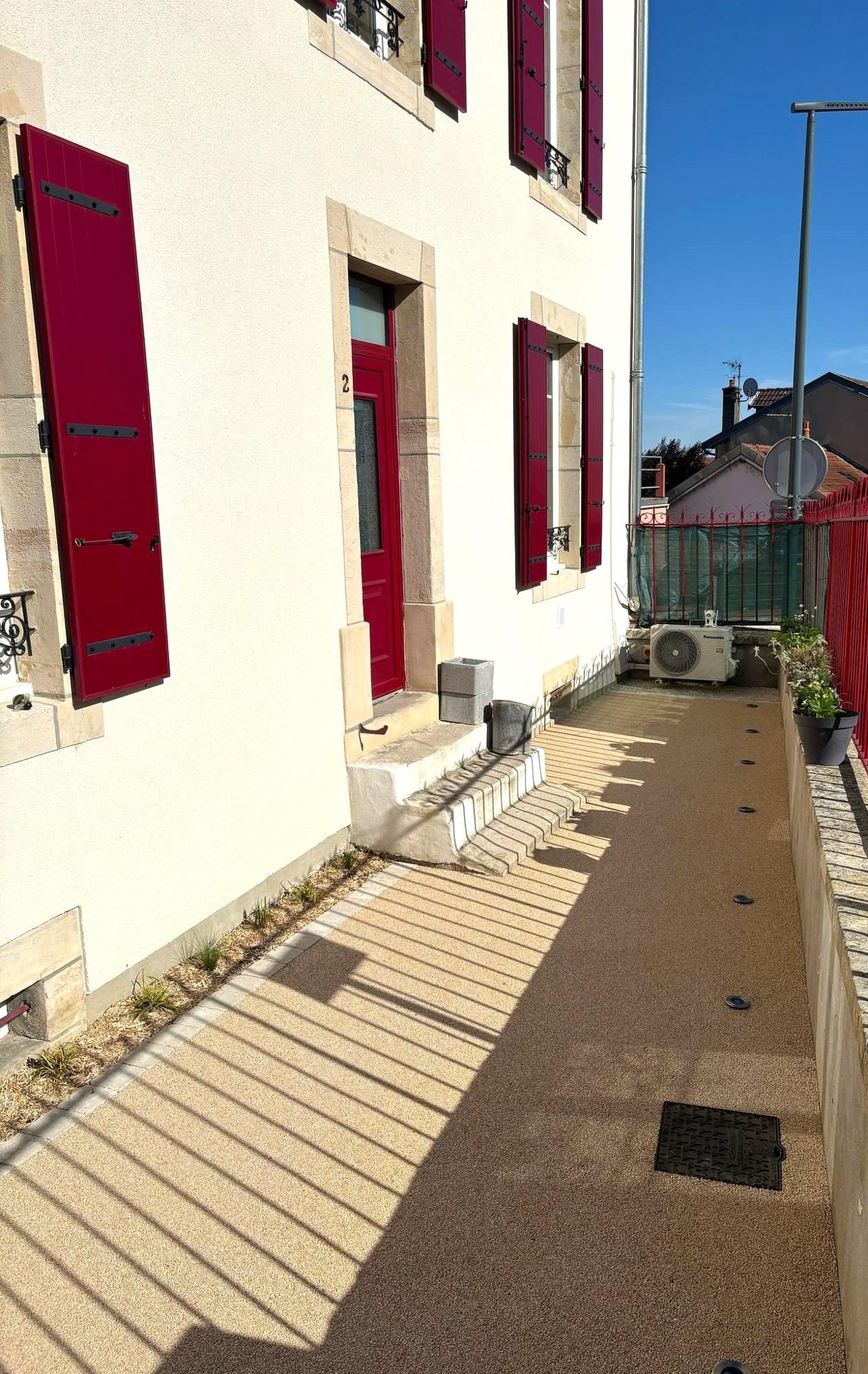 Passage gravillonné le long d'une façade aux volets rouges